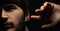 Close-up of man with wireless earphone in ear, touching this with hand. Dramatic dark portrait of young guy on black background.