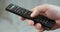 Close up mans hand holding TV remote control and changing TV channels