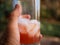 Close up of a mans left hand holding a pint class with a drink with ice outside