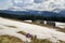 Close-up of marvelous blooming first crocuses breaking through snow. Blurred image of shepherds huts and mighty mountains covered