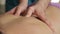 Close-up of massage therapist spends thumbs along spine on female back.