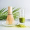 Close up of matcha espresso in glass with whisk and matcha powder on table at light background, front view with copy space. Clean