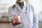 Close up mature doctor wearing uniform holding pink piggy bank