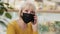 Close-up mature serious caucasian businesswoman in medical mask talking on phone answering mobile call discussing