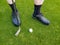 Close-up of men`s feet in black shoes and socks on a Golf course with a Golf club and a white ball