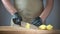 Close-up of men\'s hands in black disposable gloves. The cook is slicing potatoes on a cutting board. Background in blur.