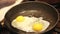 Close up of messy egg being cracked open and fried in a saucepan.