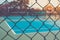 Close up metal fence with empty outdoor blue tennis hard court in the background.