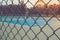 Close up metal fence with empty outdoor blue tennis hard court in the background.