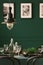 Close-up of a metal lamp hanging above an elegant table with green cloth. Blurred wall with photos in the background. Real photo