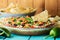 Close up of a Mexican layered dip with a bowl of nacho chips in behind.