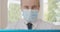 Close-up of mid-adult doctor in face mask talking at laptop selfie camera. Portrait of confident serious Caucasian man