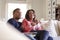 Close up of middle aged couple sitting on the sofa in their living room watching TV, laughing and eating popcorn, close up