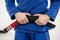 Close up on midsection of unknown caucasian male athlete bjj brazilian jiu-jitsu black belt standing on the mat at academy holding