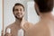 Close up mirror reflection overjoyed young man applying aftershave lotion