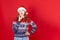 Close up of mischievous young woman in Christmas sweater and Santa hat looking sideways, copy space on red background