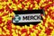 Close up of mobile phone screen with logo lettering of Merck pharmaceutical company on pile yellow red drug capsules