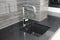 A close-up on a modern kitchen tiled up with gray ceramic wall tile with a curved line design  black kitchen countertop  square