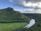 Close up of a mountain river with a boat sailing round high round mountain covered with trees on the horizon. kamokila hawaiian