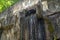 Close up of mountain stream flowing from rock in summertime. Manmade decorative waterfall flows down.