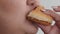Close up of the mouth of a plump young woman who takes a bite and chaos a piece of hamburger with gusto. The concept is