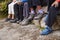 Close up of muddy shoes and trousers of a family sitting on stones by a lake, detail