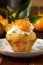 Close-up of muffin with cream, mandarin jam and decorative leaf on flower plate with tangerines in background, selective focus,