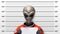 Close-up mugshot of a stereotypical gray-skinned, large-eyed alien wearing an orange spacesuit, standing against a height