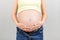 Close up of naked pregnant woman`s belly wearing opened jeans at colorful background with copy space. Pregnancy concept