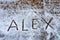 Close up at name Alex which is written is in capital letters on hailstones at wooden terrace during hailstorm from sky with