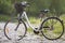 Close-up of new modern white bicycle with black wheels and basket standing on side stand on lit by sun pebbles on blurred green s