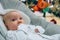 Close up on newborn baby looking into camera, christmas tree in background