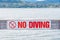 Close-up of No Diving sign on pier with view of Okanagan Lake and mountains in background