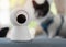 Close up object shot of a modern Wi-Fi surveillance camera set in the room with dog is sitting on a sofa in the Background