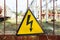 Close-up old aged rusty triangle metal plate with High voltage warning sign. Power station with transformers and