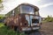 Close-up of old forsaken passenger bus with broken windows rusting in high green weedy grass on edge of plowed brown field on brig