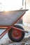 Close-up of an old gardening wheelbarrow. Aluminum wheelbarrow is red. Sunset is in the background. The wheelbarrow is