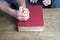 Close-up of old man`s hands folded in prayer gesture on thick family bible in dark red cover, concept of eternal Christian values