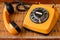 Close up of an old, scratched orange rotary dial telephone with the receiver left open on a bamboo mat