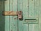 Close up of an old wooden door with green faded paint and a rusty closed padlock and old metal letterbox