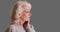 Close up of older woman with headache touching her temples on grey background