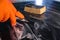 Close-up of an orange glove with a metal scraper cleaning the cooktop. Selective Focus. A yellow sponge lies in the background.