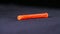 Close-up of orange plastic dowel. Stock footage. Single orange dowel lies on black background. Dowel is used in