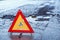 Close up of an orange triangle road sign in the background of a broken asphalt road and puddle