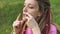 Close-up outdoors portrait of young female shaman in pink knitted sweater with long dreadlocks playing on traditional