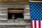 Close up of outside wall of rustic wood building, open window with dusty lantern on windowsill, American flag hanging on wall
