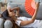 Close up overheated woman waving paper fan, lying on couch