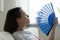 Close up overheated young woman waving blue paper fan