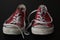 Close up of pair of sneakers - red and white vintage worn out shoes - youth hipster shoes on black background