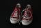 Close up of pair of sneakers - red and white vintage worn out shoes - youth hipster shoes on black background - top view